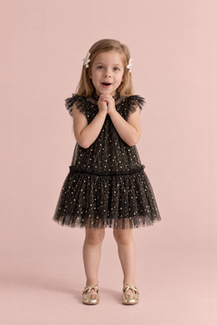 Stardust Black Star Tulle Party Dress, front: a girl with her hands clasped under her chin in the black tulle dress with gold stars and flutter sleeves
