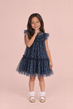 Stardust Navy Star Tulle Party Dress, front: a girl with a finger to her lips in the navy tulle dress with gold stars and flutter sleeves