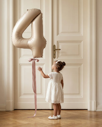 Little girl reaching for a champagne number balloon, The Birthday Edit