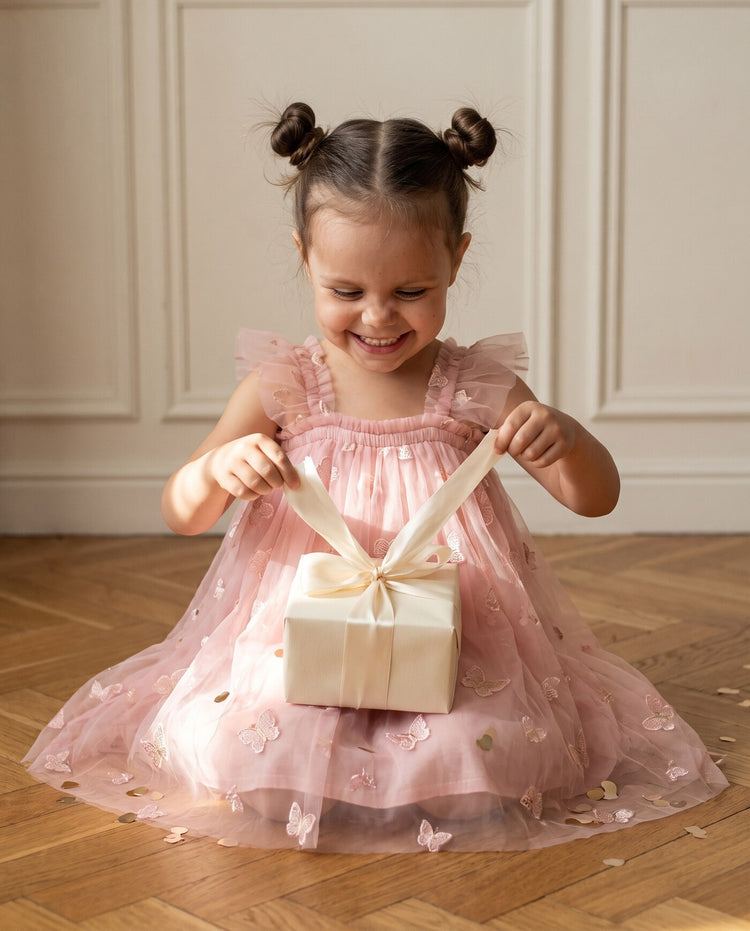 Little girl in a pink butterfly tulle dress untying the ribbon on a small gift