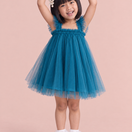 Girl wearing the Papillon Teal Butterfly Back Flower Girl Dress, front, arms curved up overhead like a ballerina