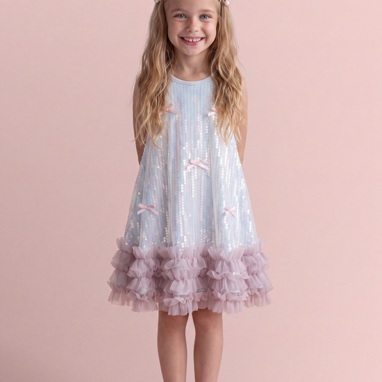 Periwinkle blue sequin party dress, front view on a girl, iridescent sequin swing dress with pink bows and a pink ruffle hem