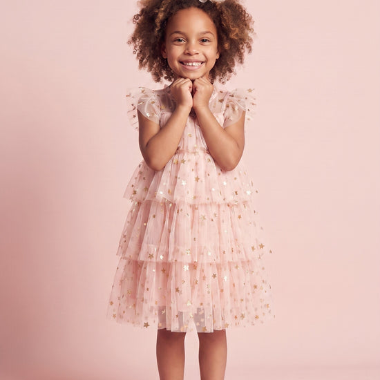 Girl wearing the Petal Star Dress in blush pink star tulle, front
