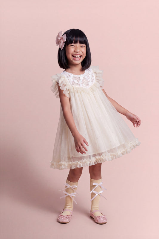 Girl wearing the Primrose Ivory Crochet Flower Girl Dress, white crochet yoke scattered with tiny gauze roses over sheer glitter tulle