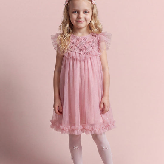 Girl wearing the Primrose pink crochet flower girl dress, front view, with a rose covered yoke over sheer glitter tulle