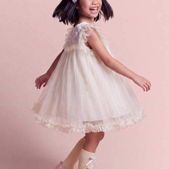 Side view of the Primrose ivory dress mid twirl, the tulle skirt flaring into a full bell