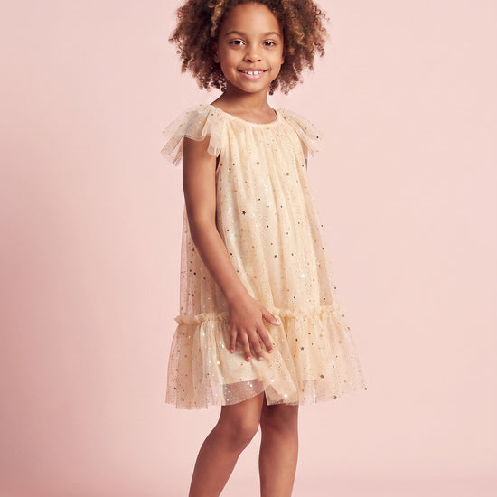 Girl wearing the Starlight Dress in cream gold star tulle, front