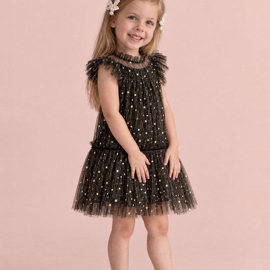 Stardust Black Star Tulle Party Dress, three quarter view, smoothing her skirt with both hands, showing the ruffle collar and drop waist skirt
