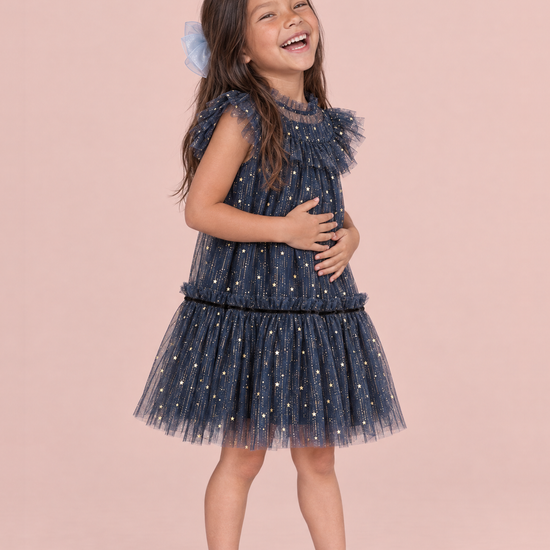Stardust Navy Star Tulle Party Dress, three quarter view, laughing with her hands on her tummy, showing the ruffle collar and drop waist skirt